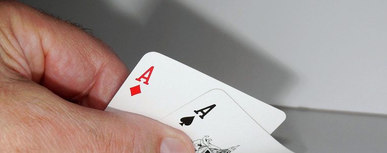 Two aces held in a hand above a table